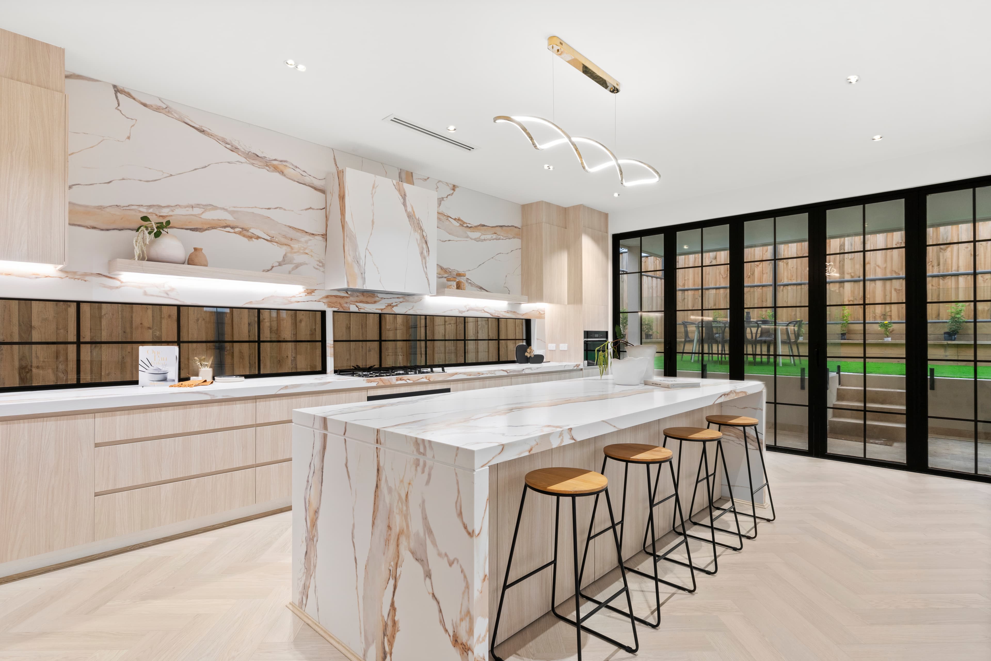 Luxury kitchen with a Calacatta marble waterfall island, timber cabinetry and gold pendant lighting by Reno Build on Sydney's Northern Beaches