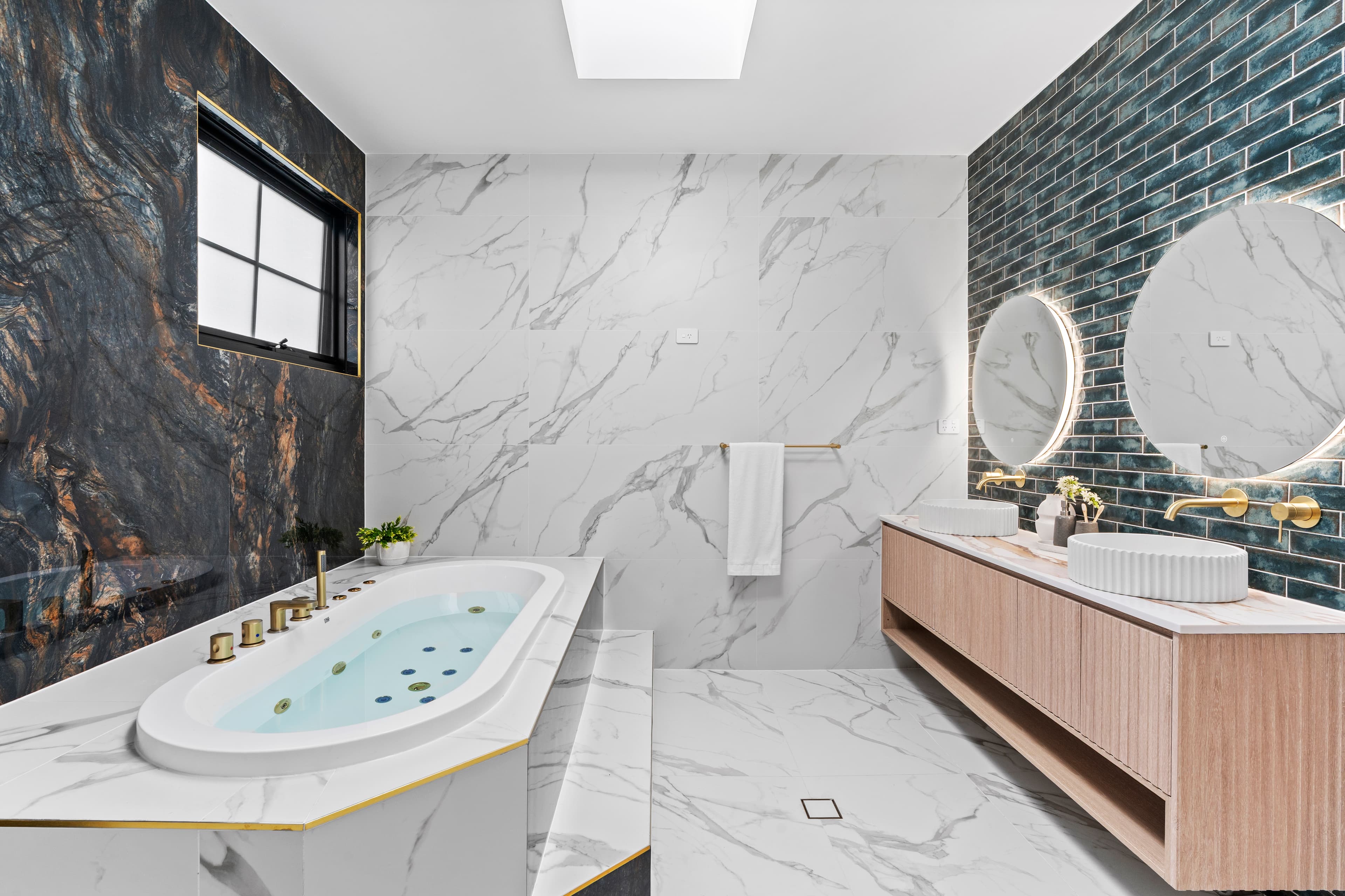Luxury spa bathroom with a dark marble feature wall, freestanding bath and gold fittings by Reno Build on Sydney's Northern Beaches