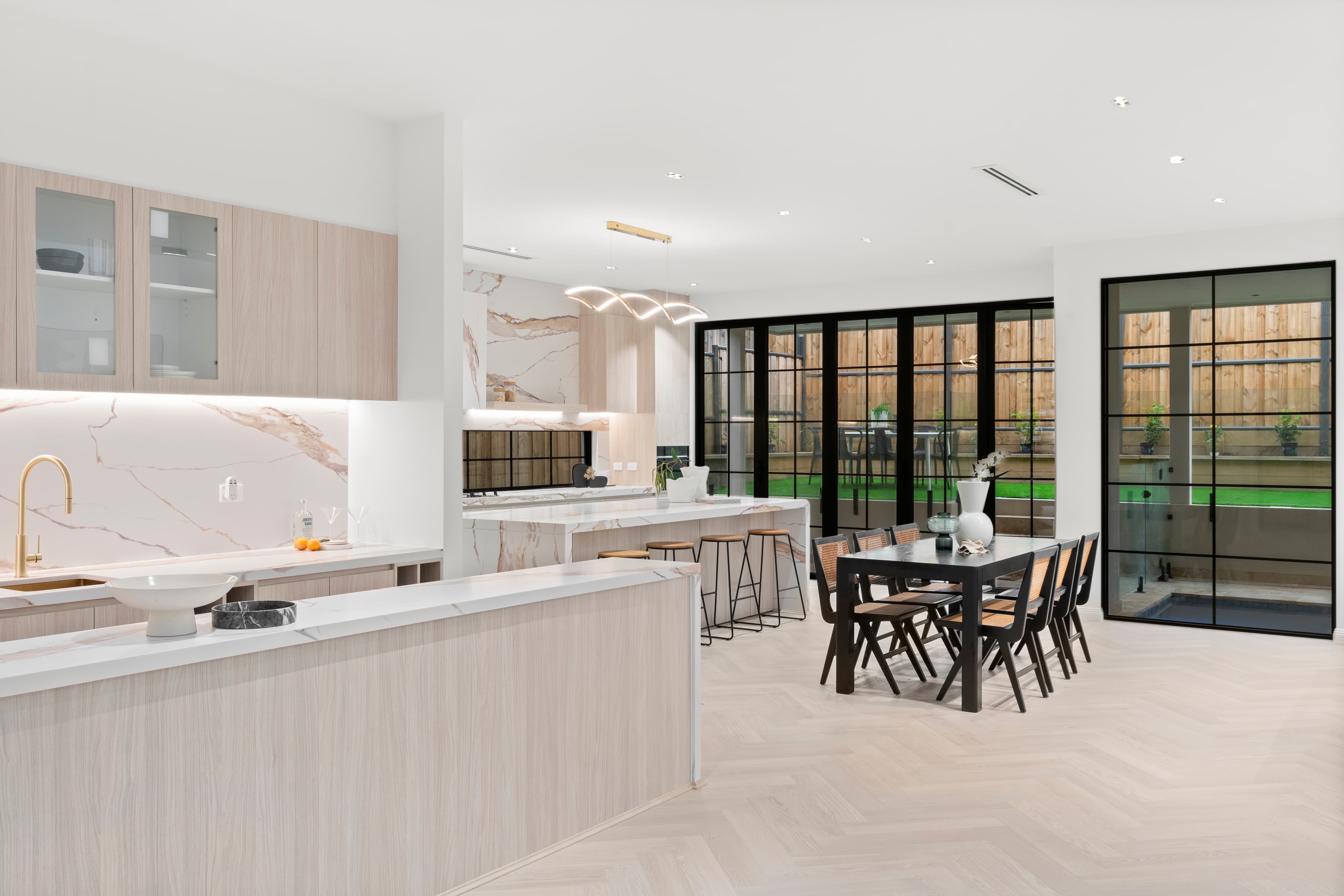 Open-plan kitchen and dining renovation with marble benchtops and black-framed windows by Reno Build on Sydney's Northern Beaches