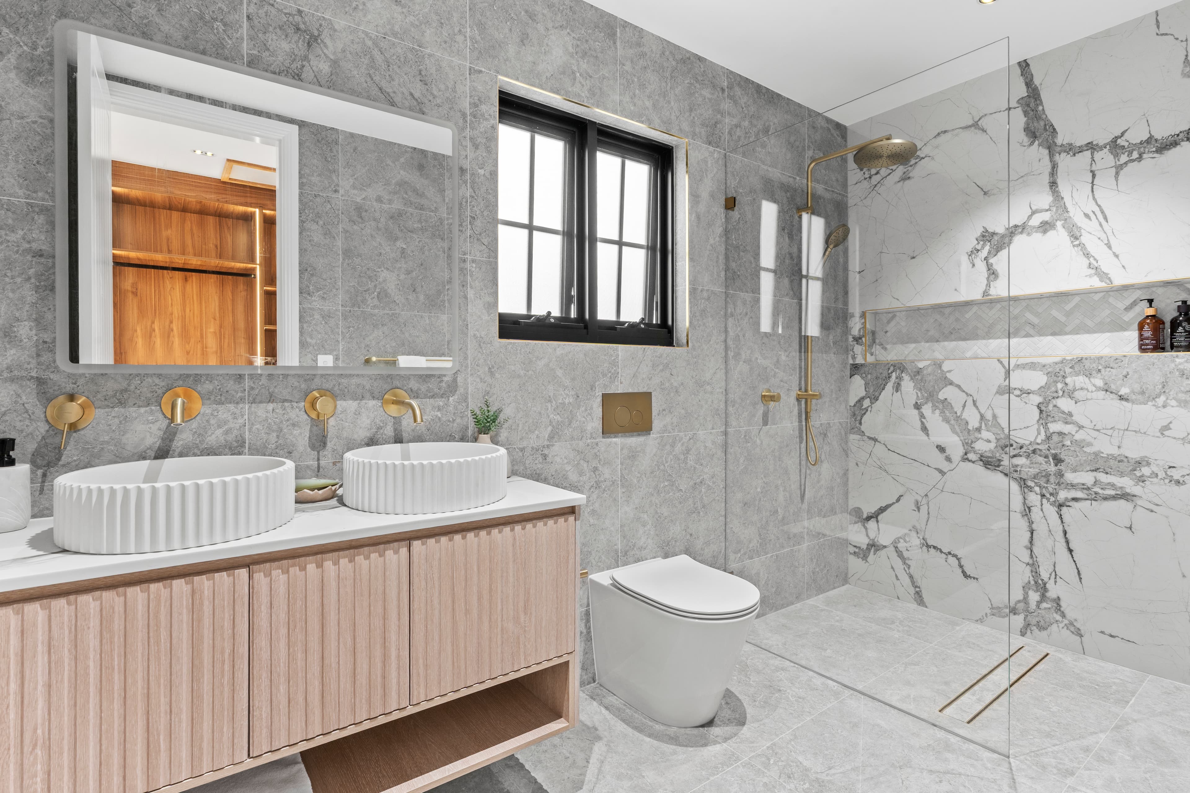 Renovated family bathroom with double vanity, brushed gold tapware and grey marble tiles by Reno Build on Sydney's Northern Beaches
