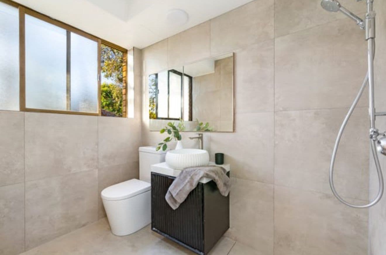 Renovated laundry with large-format concrete-look tiles and matte black joinery by Reno Build on Sydney's Northern Beaches